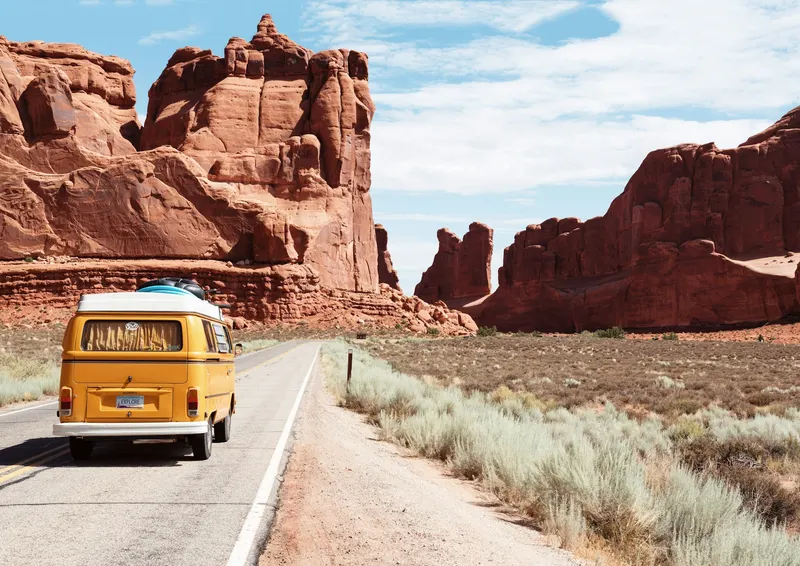 A vintage yellow van traveling along a road between red rock formations
